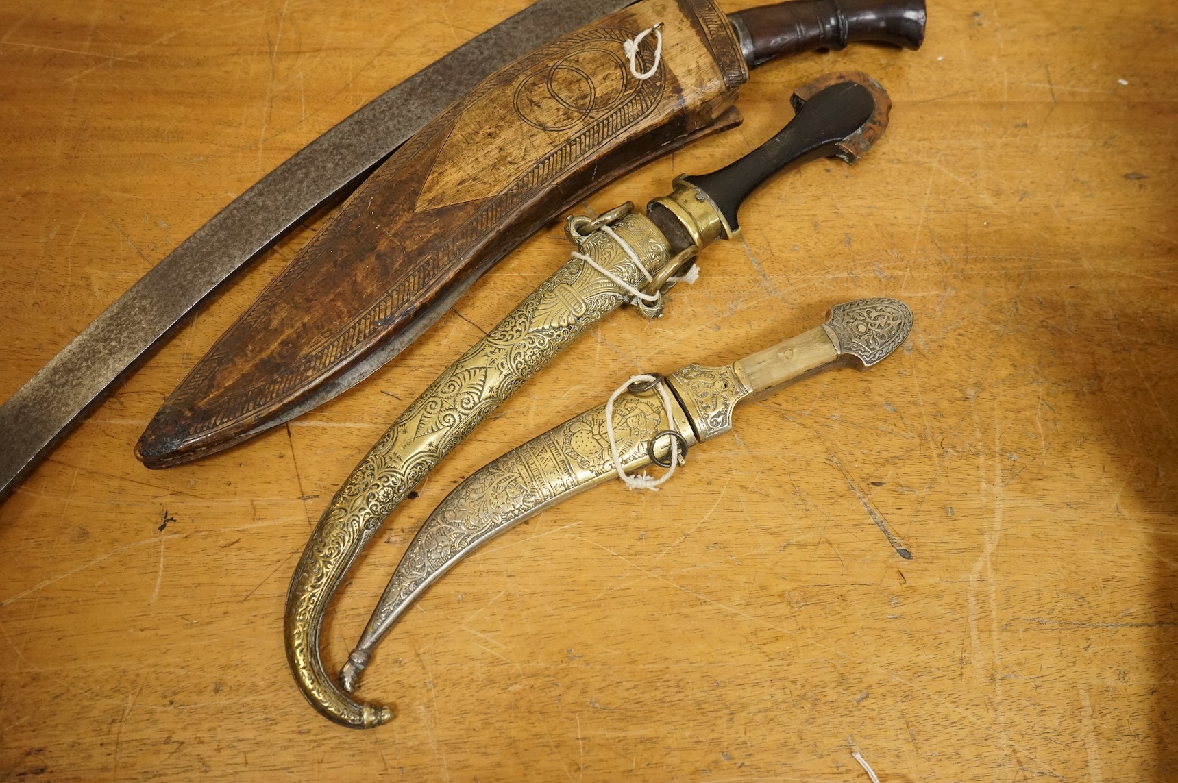 An Indian sword tulwar, the iron hilt with traces of chiselled and inlaid decoration, together with a kukri in its wooden scabbard, a Syrian jambya and a Moroccan jambiya (4)